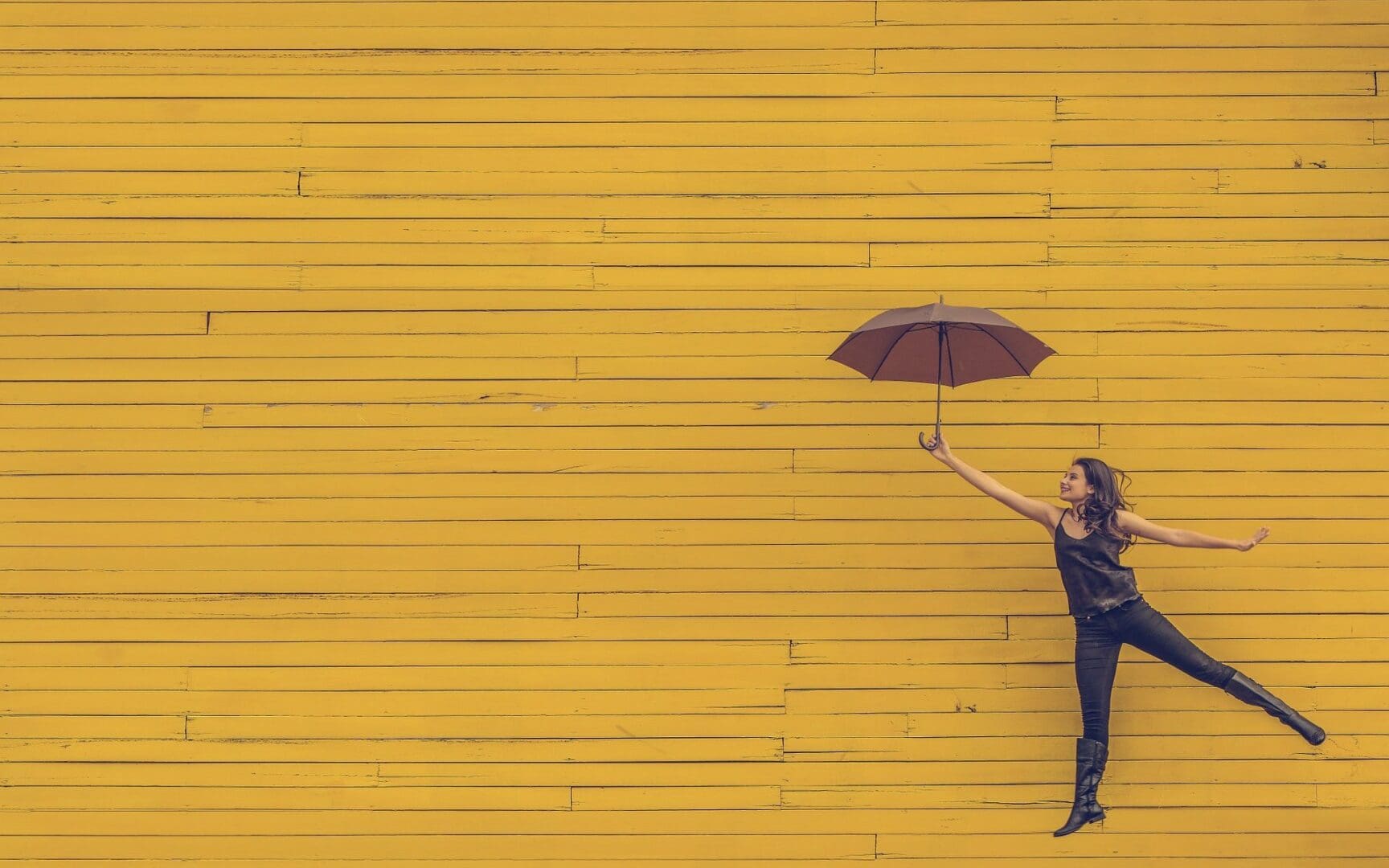 Person holding umbrella against yellow wooden background.