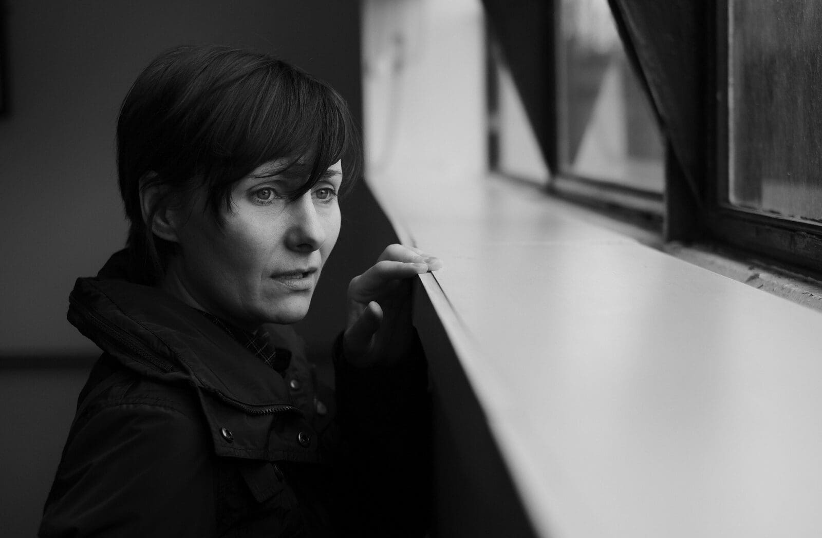 Person looking out a window, monochrome scene.