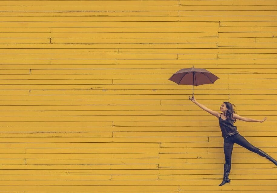 Person holding umbrella against yellow wooden background.